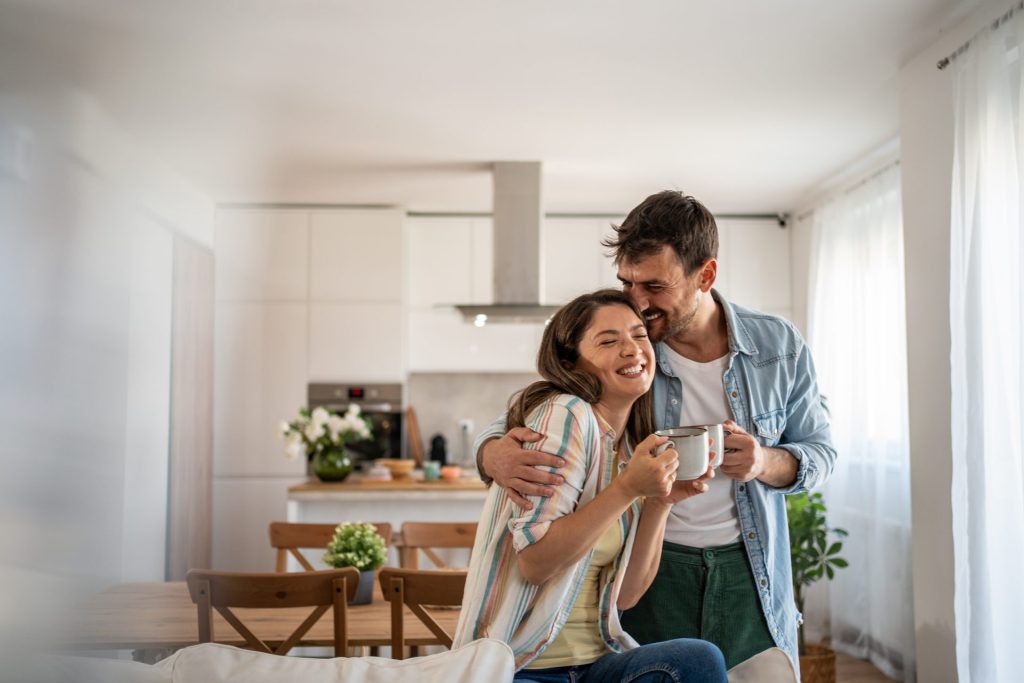 Couple hugging with coffee mugs in bright kitchen