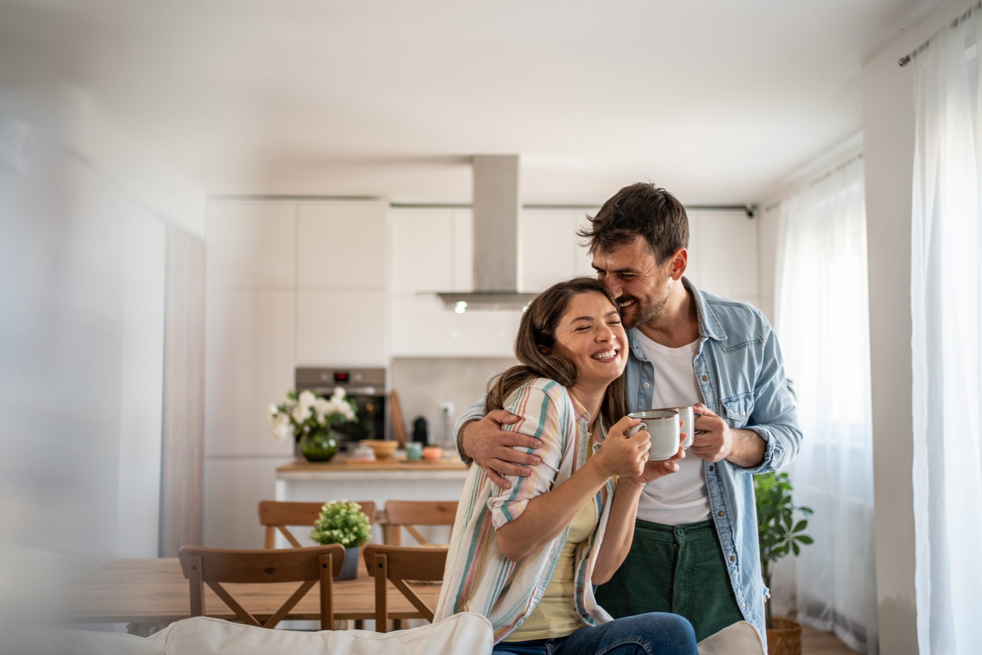 Couple hugging with coffee mugs in bright kitchen