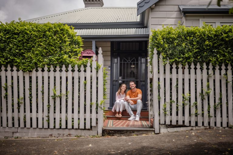 Couple sitting on front steps behind picket fence