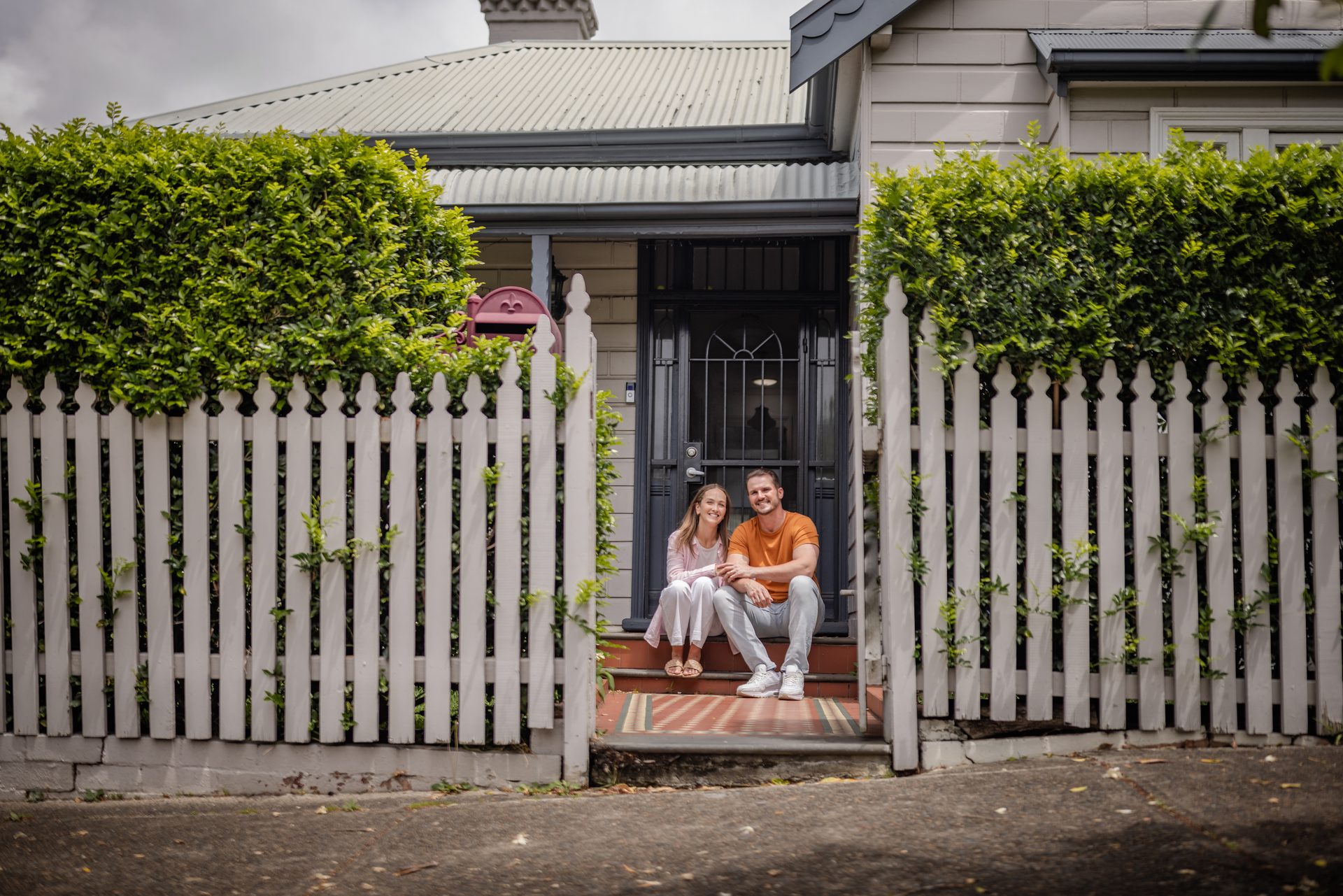 Couple sitting on front steps behind picket fence
