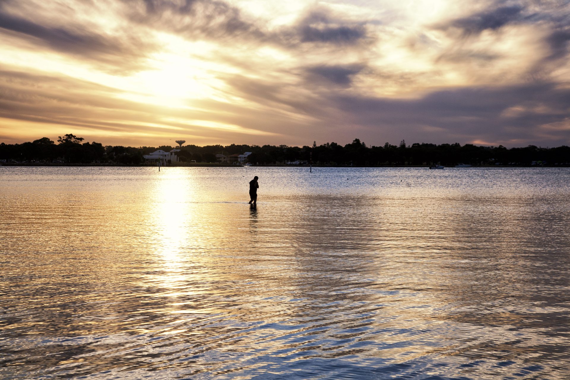 Silhouette walking through shallow water at sunset