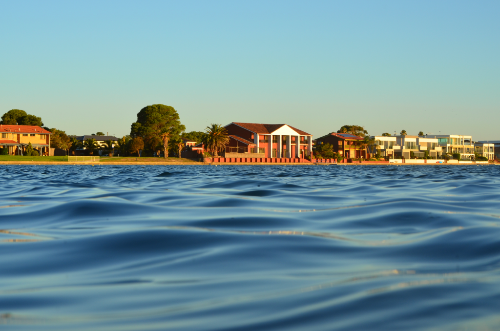 Stunning lakefront homes in West Lakes, Australia, with calm water and a clear blue sky.